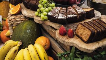 Une table en bois sur laquelle on trouve différents fruits, notamment des bananes, des oranges et des raisins, ainsi qu’une miche de pain.