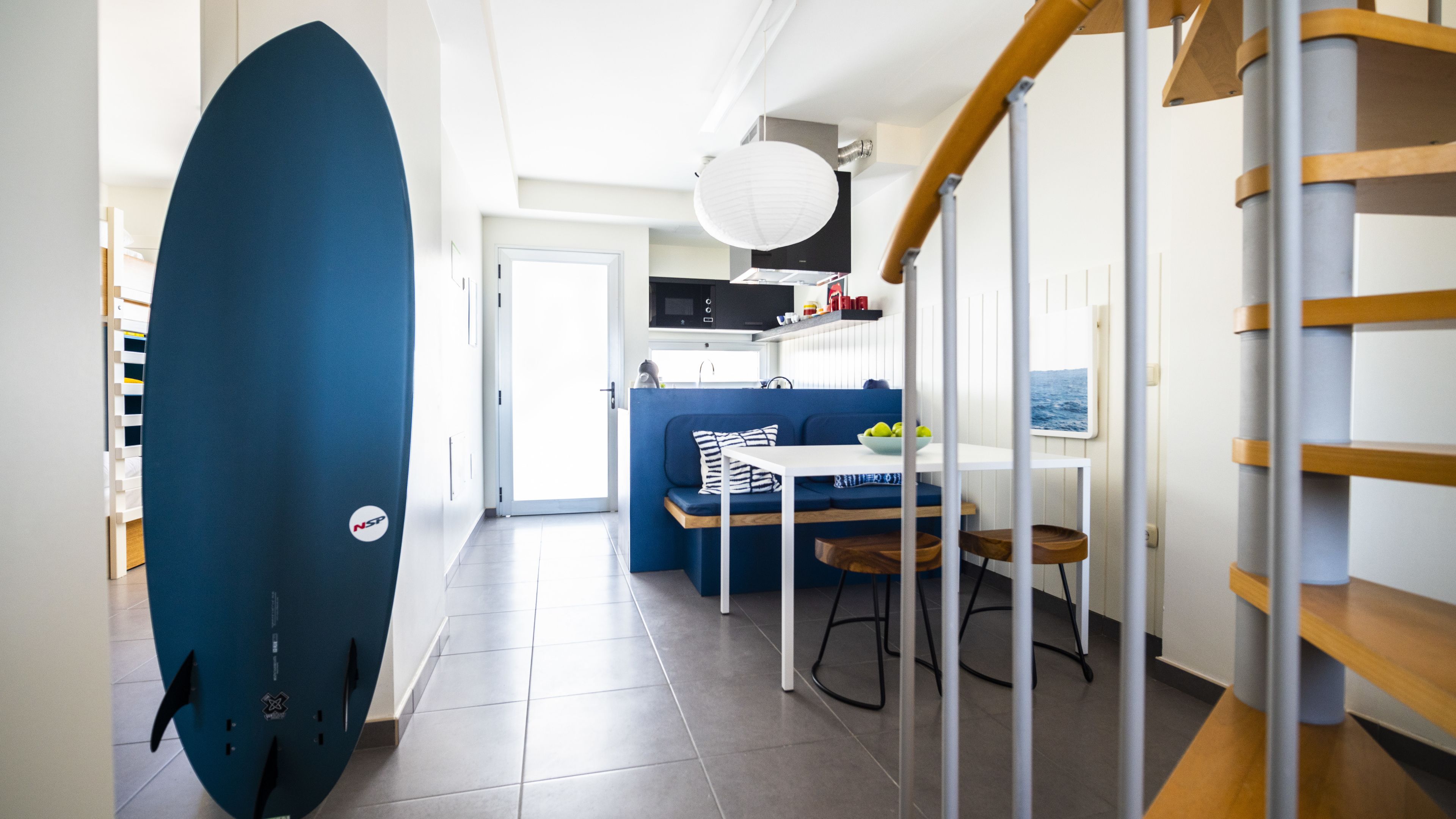 A modern kitchen with a built-in microwave, a dining area with a blue sofa, and a staircase with wooden railings.