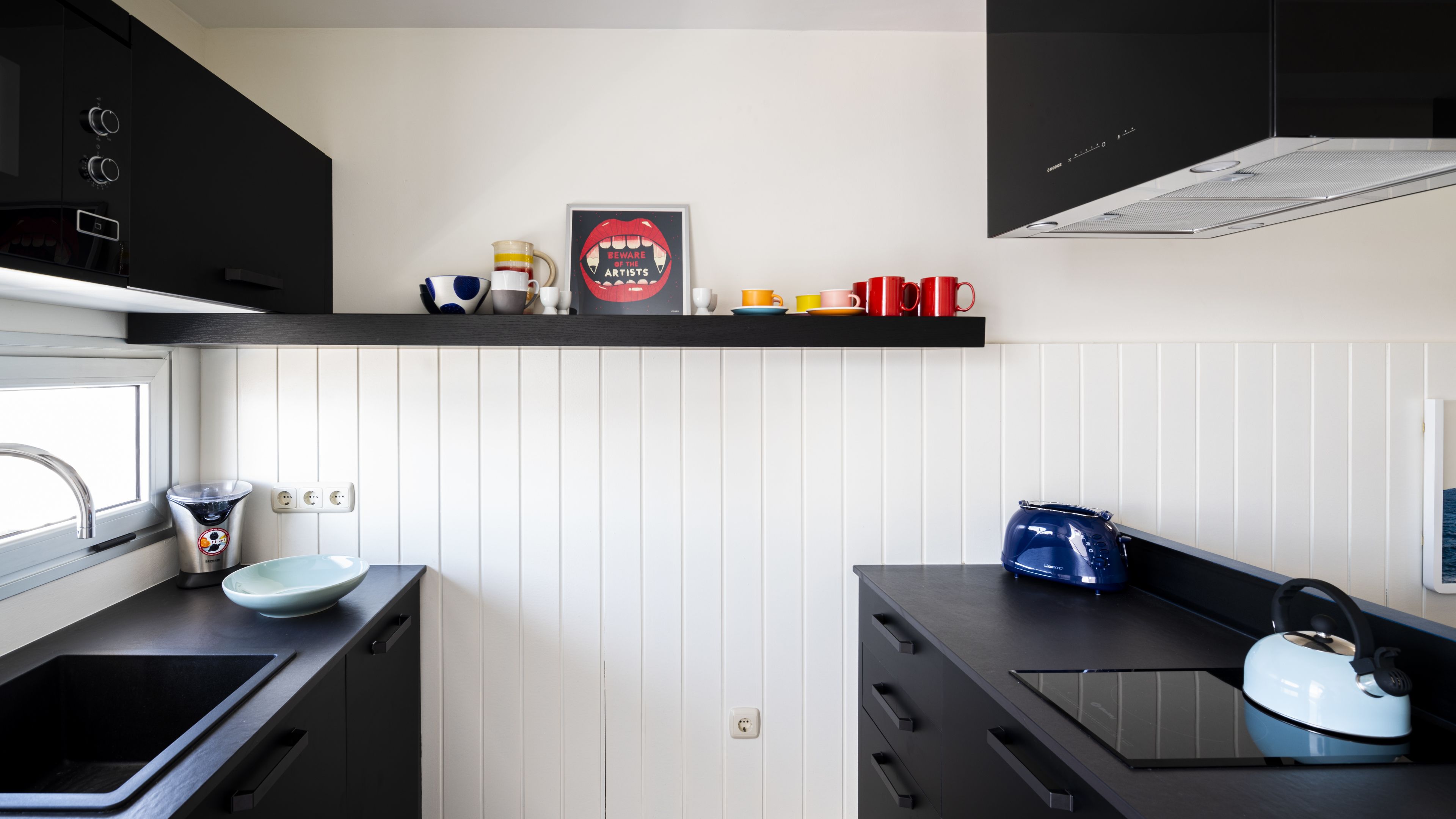 A modern kitchen with black cabinets, a white backsplash, and a stainless steel kettle.