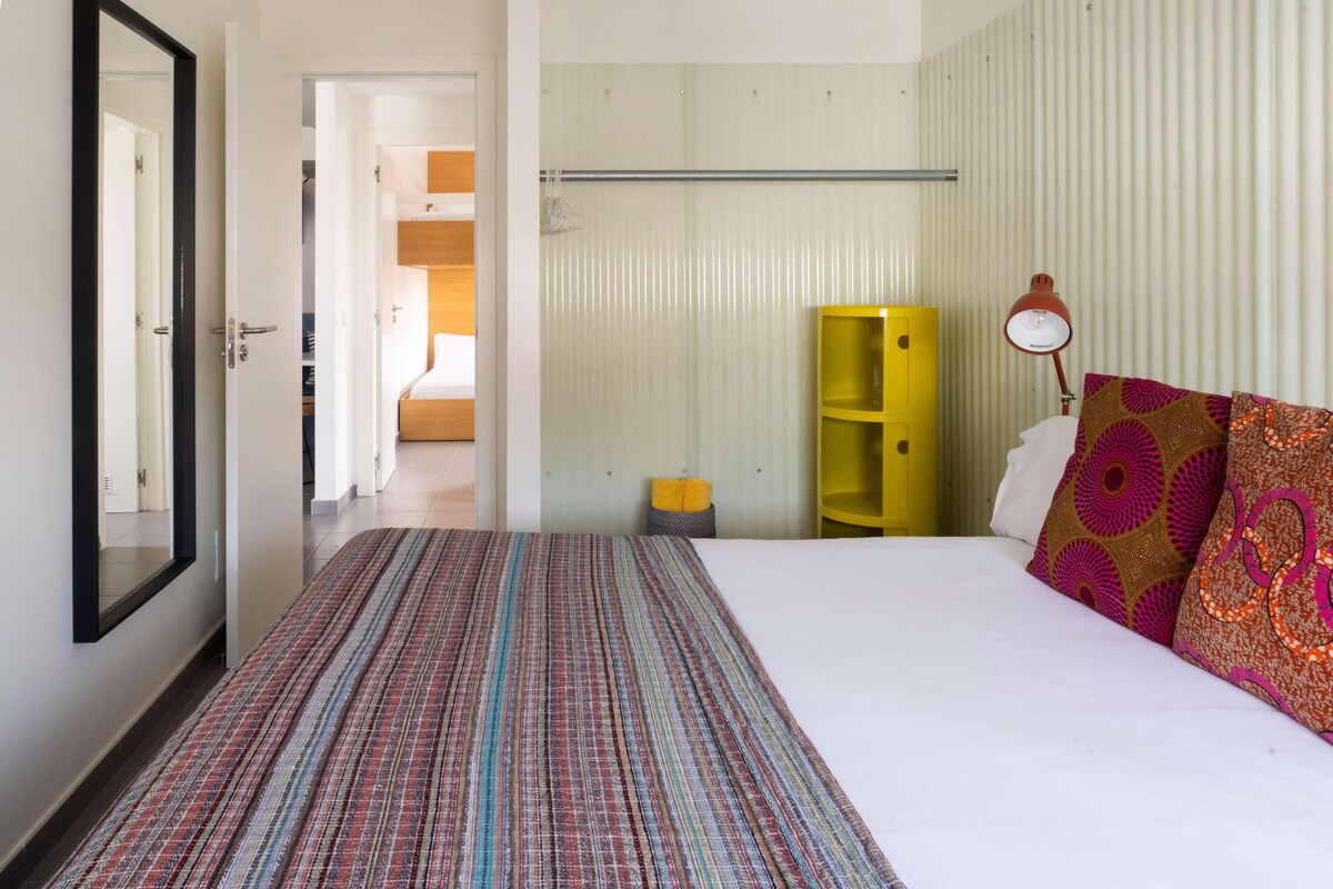 Una habitación de hotel con cama, espejo, mesita de noche, lámpara y armario.