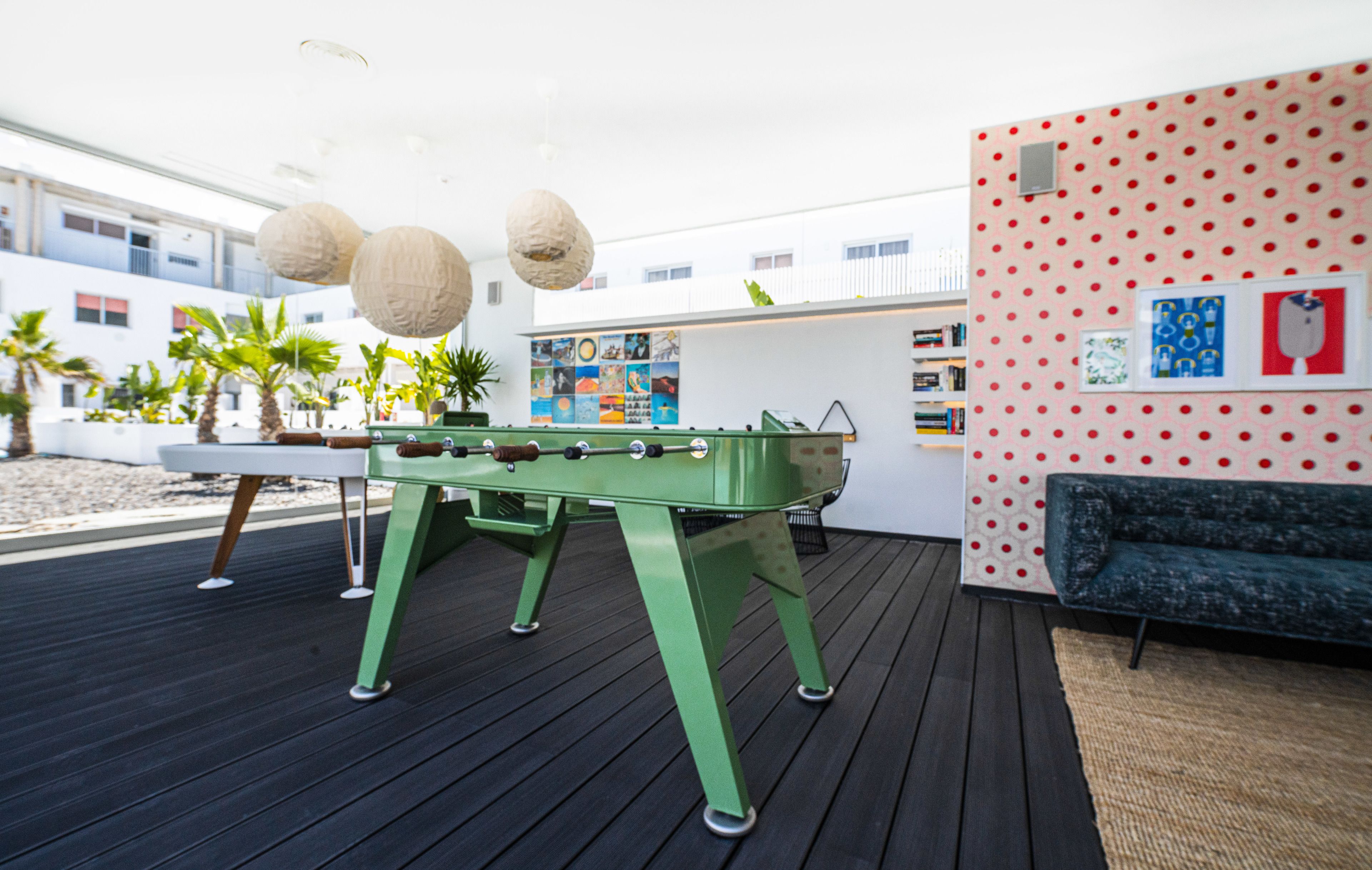 A pool table with a green table and white net, a green sofa, and a red polka dot wall with framed pictures.