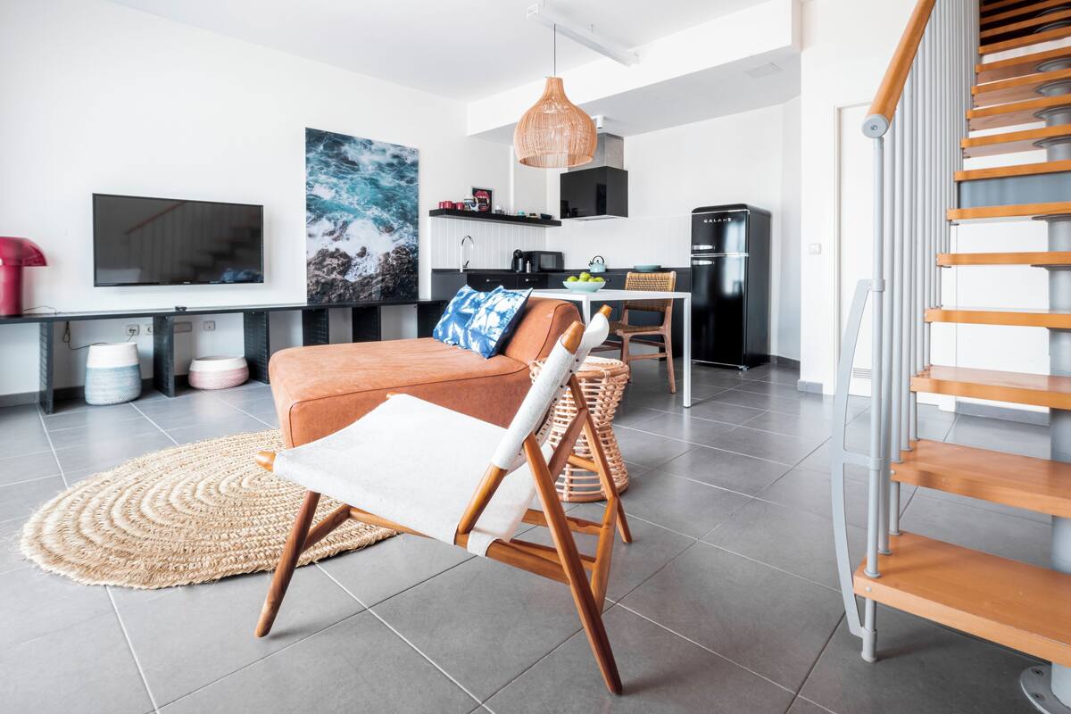 Un salon moderne comprenant un canapé, un fauteuil, un téléviseur et un coin cuisine avec un réfrigérateur et un four à micro-ondes.
