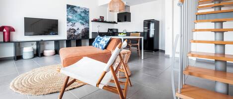 A modern living room with a sofa, a chair, a TV, and a kitchen area with a fridge and microwave.