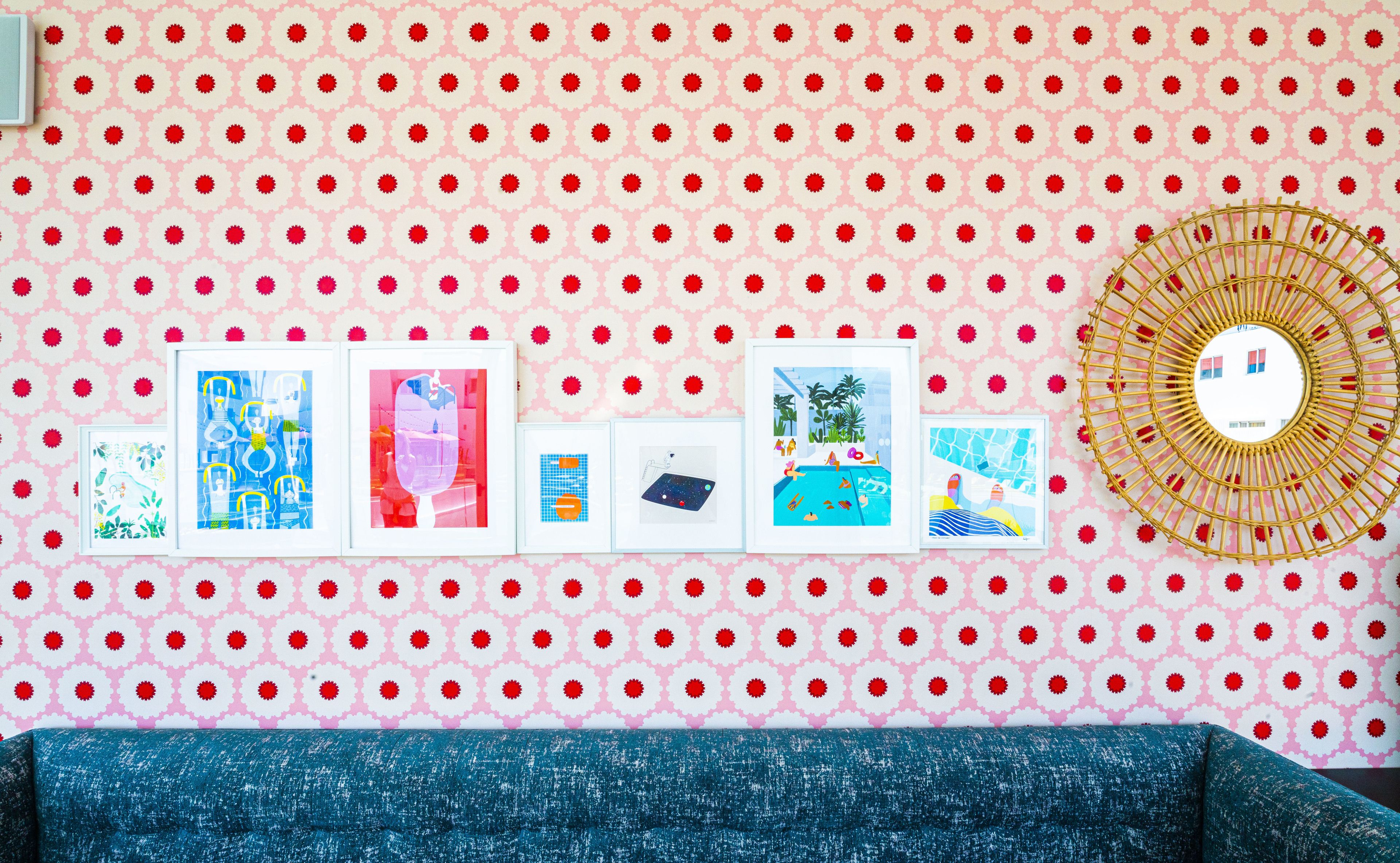 A wall with a pink and white polka dot pattern, five framed artworks, and a round mirror with a golden frame.
