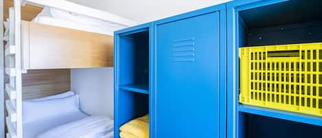 A bunk bed with white bedding and a blue wardrobe with a yellow basket.