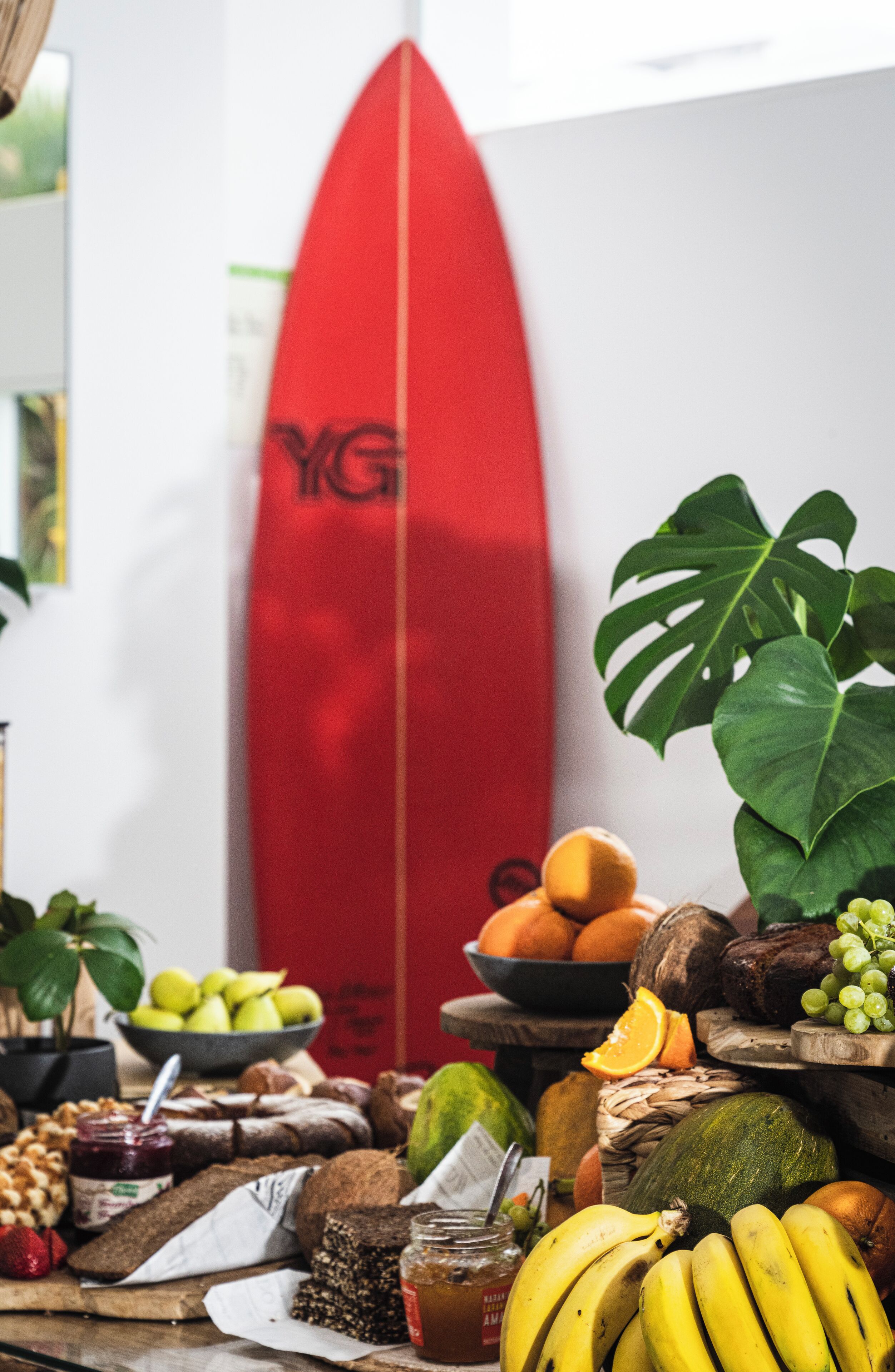 Een tafel met verschillende soorten fruit, lekkernijen, een surfboard en een plant.