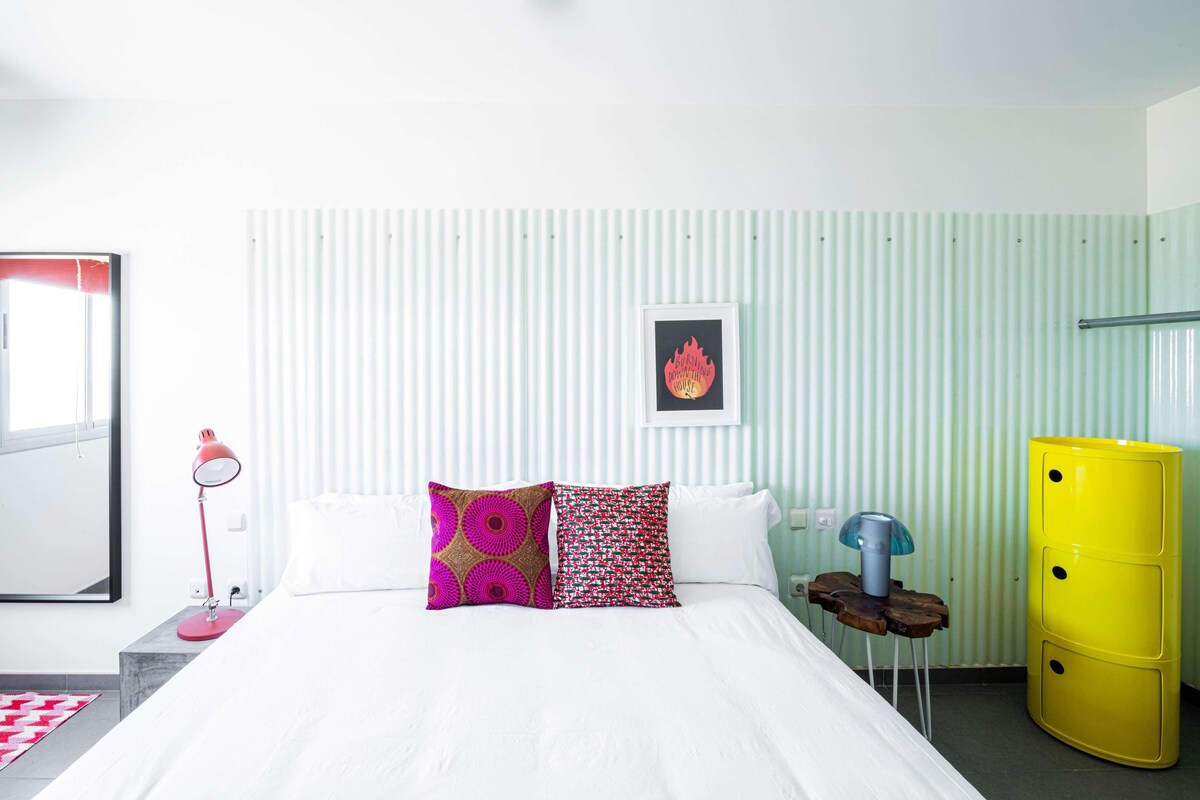 Una habitación de hotel con cama, lámpara de noche, un cuadro en la pared y un armario amarillo.