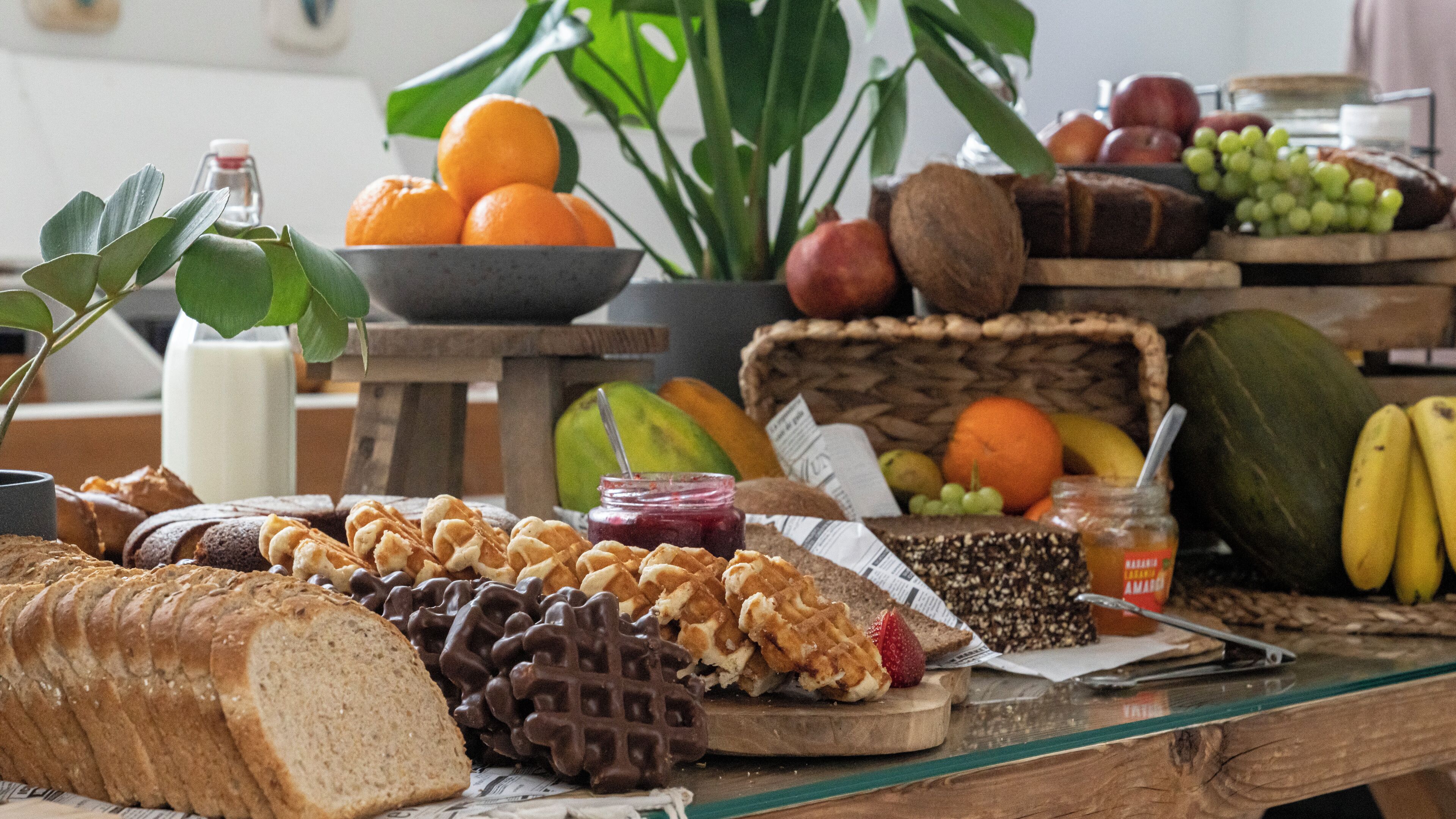 A table with various food items including bread, chocolate, fruits, and a plant.
