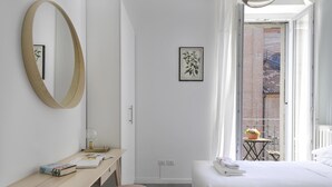 A hotel room with a bed, a desk, a mirror, a framed picture, and a view of a balcony with plants. - At Home Heart of Milan - Bright City (Milan)