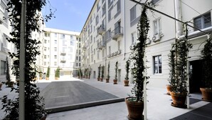 A courtyard with potted plants, a tiled floor, and a building with balconies and windows. - At Home Heart of Milan - Bright City (Milan)