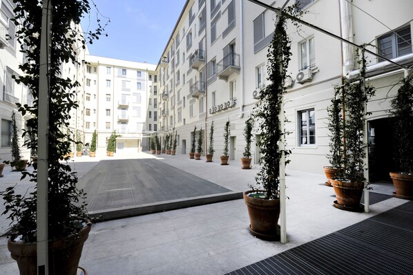 A courtyard with potted plants, a tiled floor, and a building with balconies and windows.
