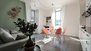 A modern living room with a sofa, a dining table with chairs, a potted plant, and a kitchen area. - At Home Heart of Milan - Bright City (Milan)