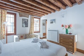 A bedroom with a wooden ceiling, a bed with white linens, a dresser, and a radiator.