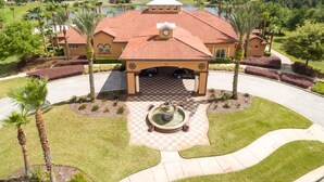A large building with a red-tiled roof, a central courtyard with a fountain, and a surrounding landscaped area with palm trees.