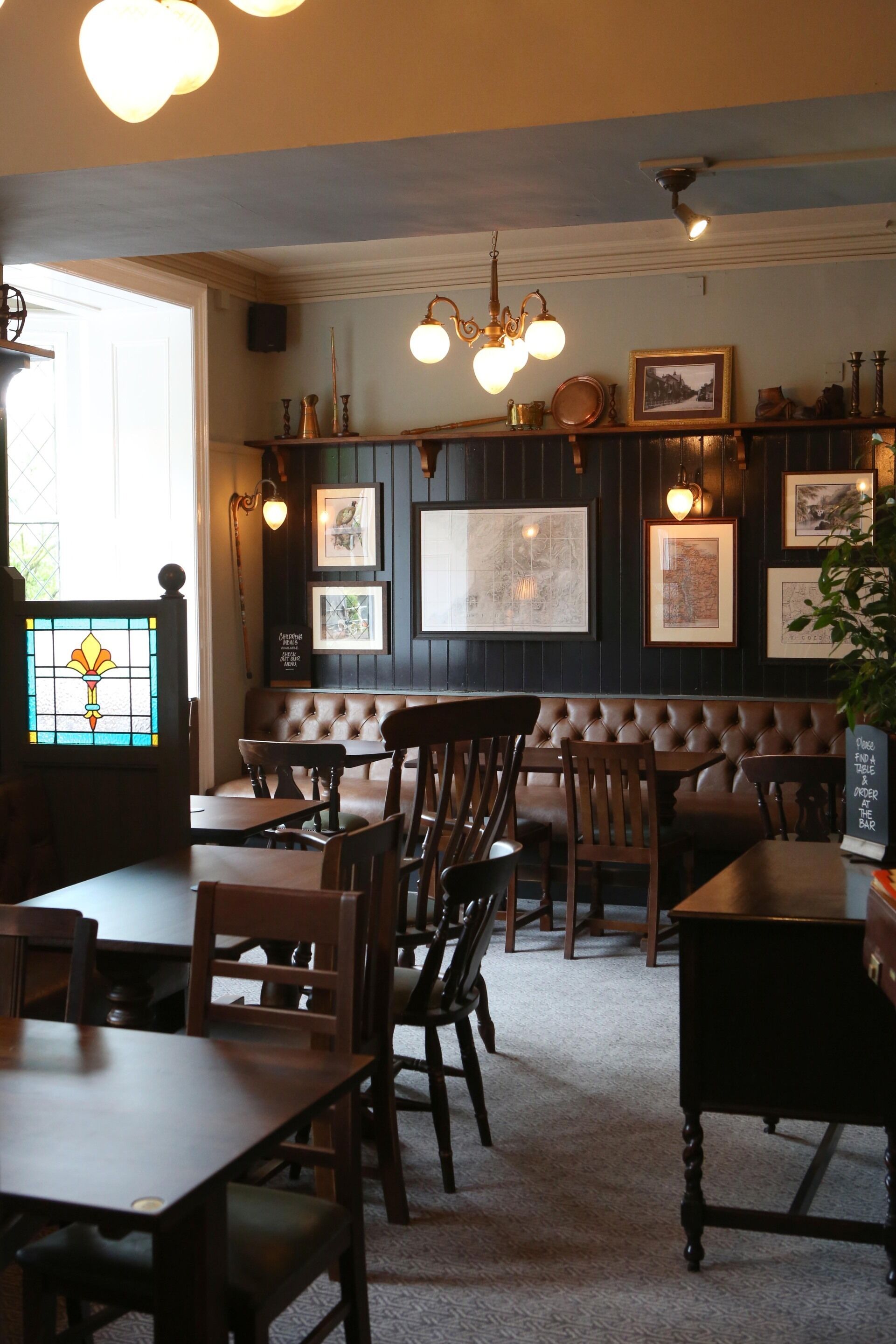 A restaurant interior with wooden tables and chairs, a cushioned bench, and wall-mounted artwork.
