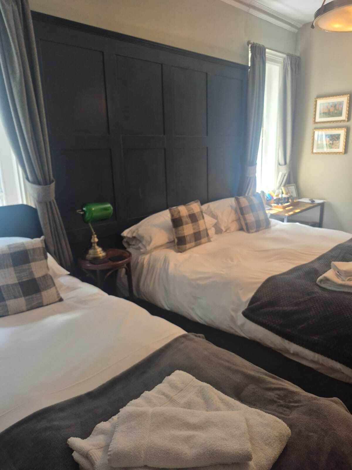 A hotel room with two beds, a nightstand with a lamp, and a window with curtains.