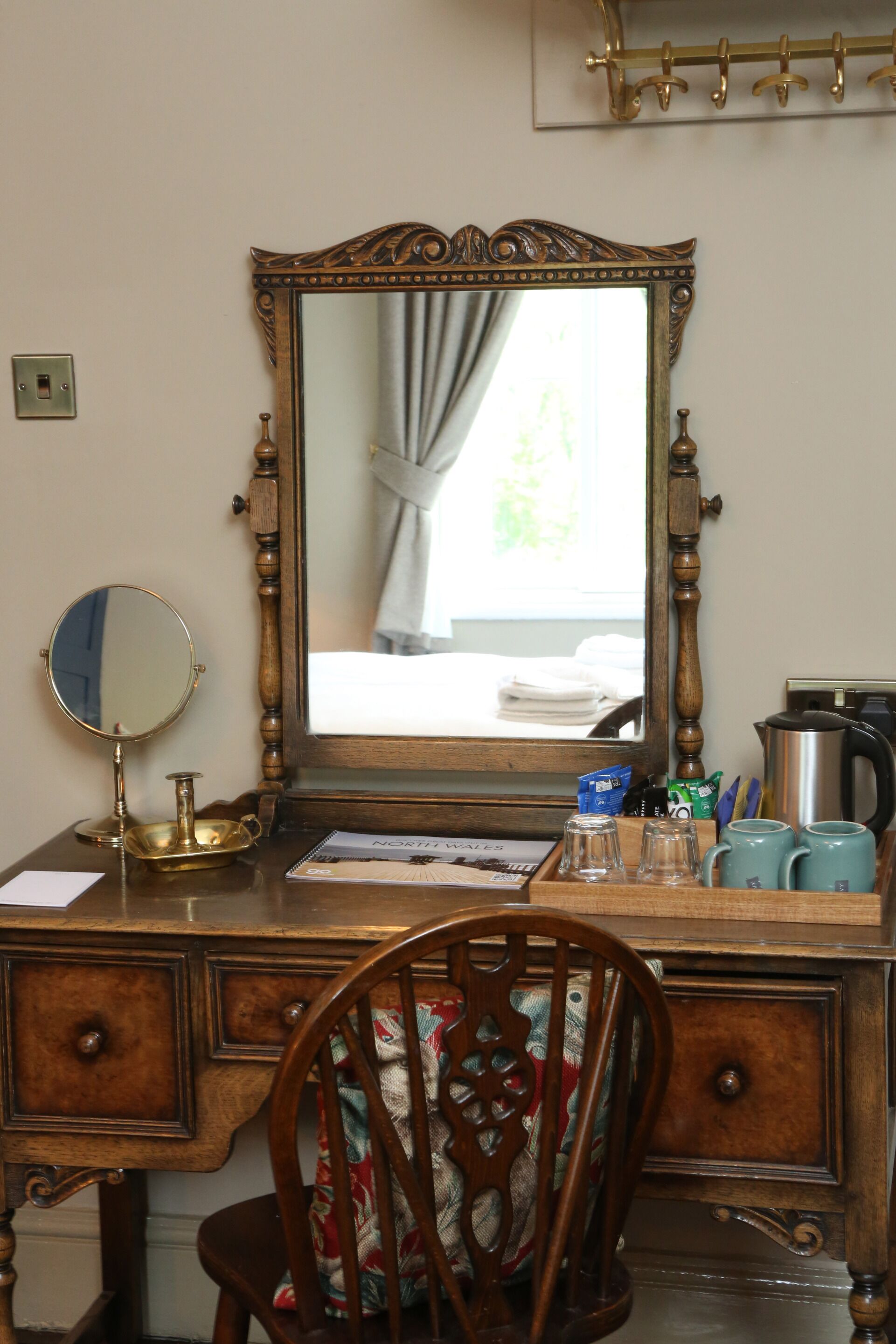 A wooden desk with a mirror, a chair, a kettle, and a coffee maker.