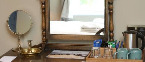 A wooden desk with a mirror, a chair, a kettle, and a coffee maker.
