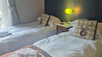 A hotel room with two beds, a dark headboard, a nightstand with a lamp, and a window with curtains.
