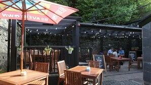 An outdoor seating area with wooden tables and chairs, a red umbrella, and a stone wall in the background. - Pont Y Pair Inn (Betws-Y-Coed)