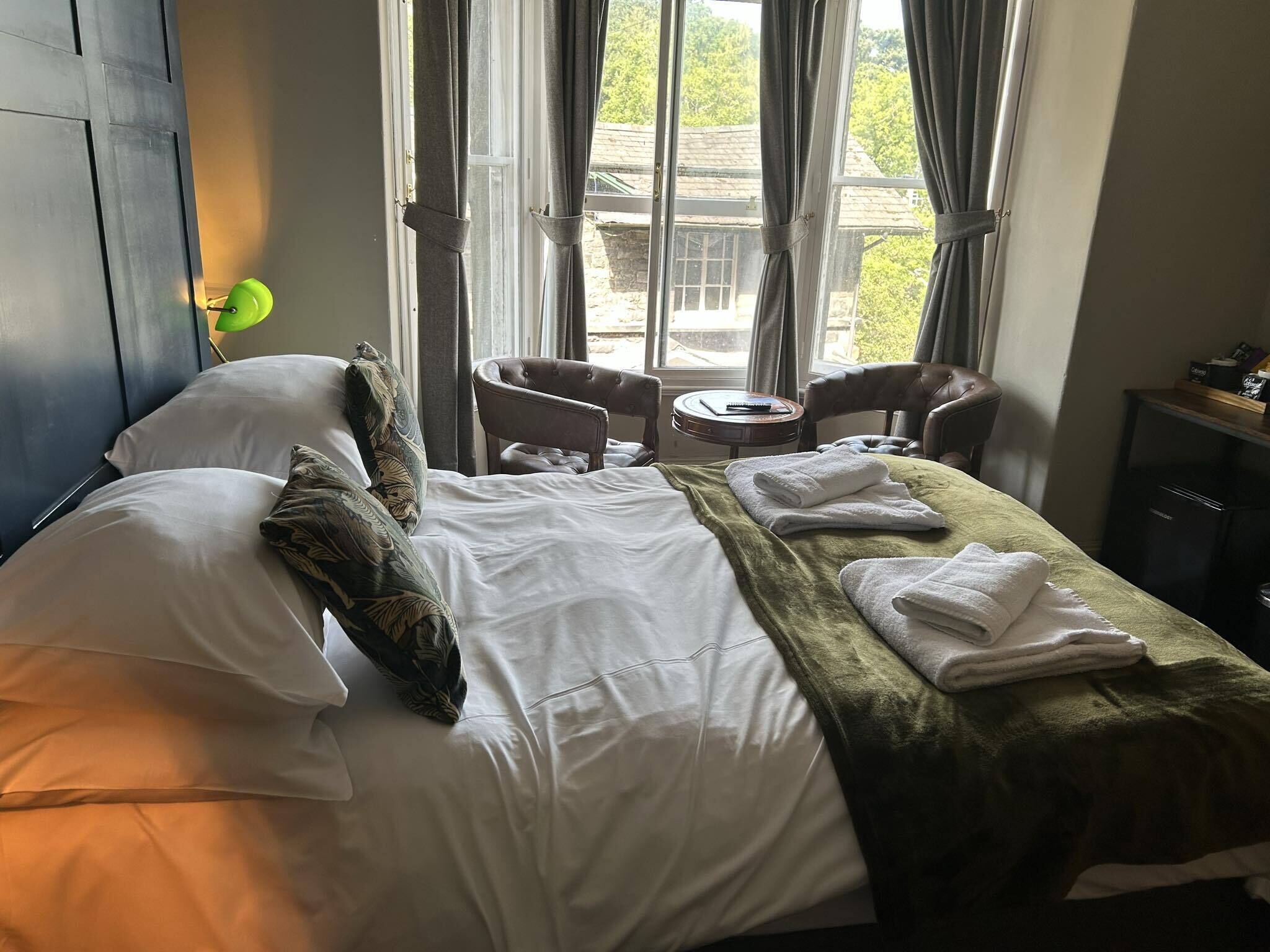 A hotel room with a bed, two chairs, a small table, and a view of the outdoors.