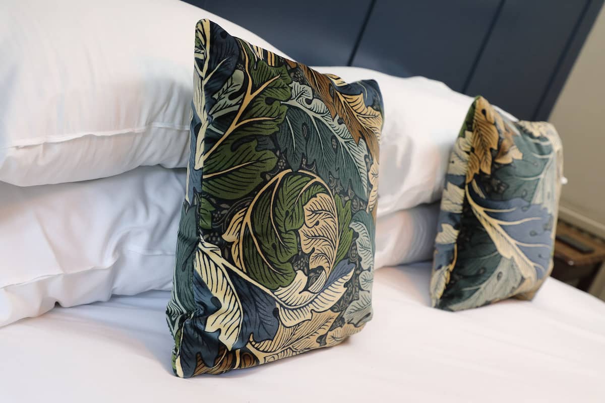 A bed with white linens and two decorative pillows with a leaf pattern.