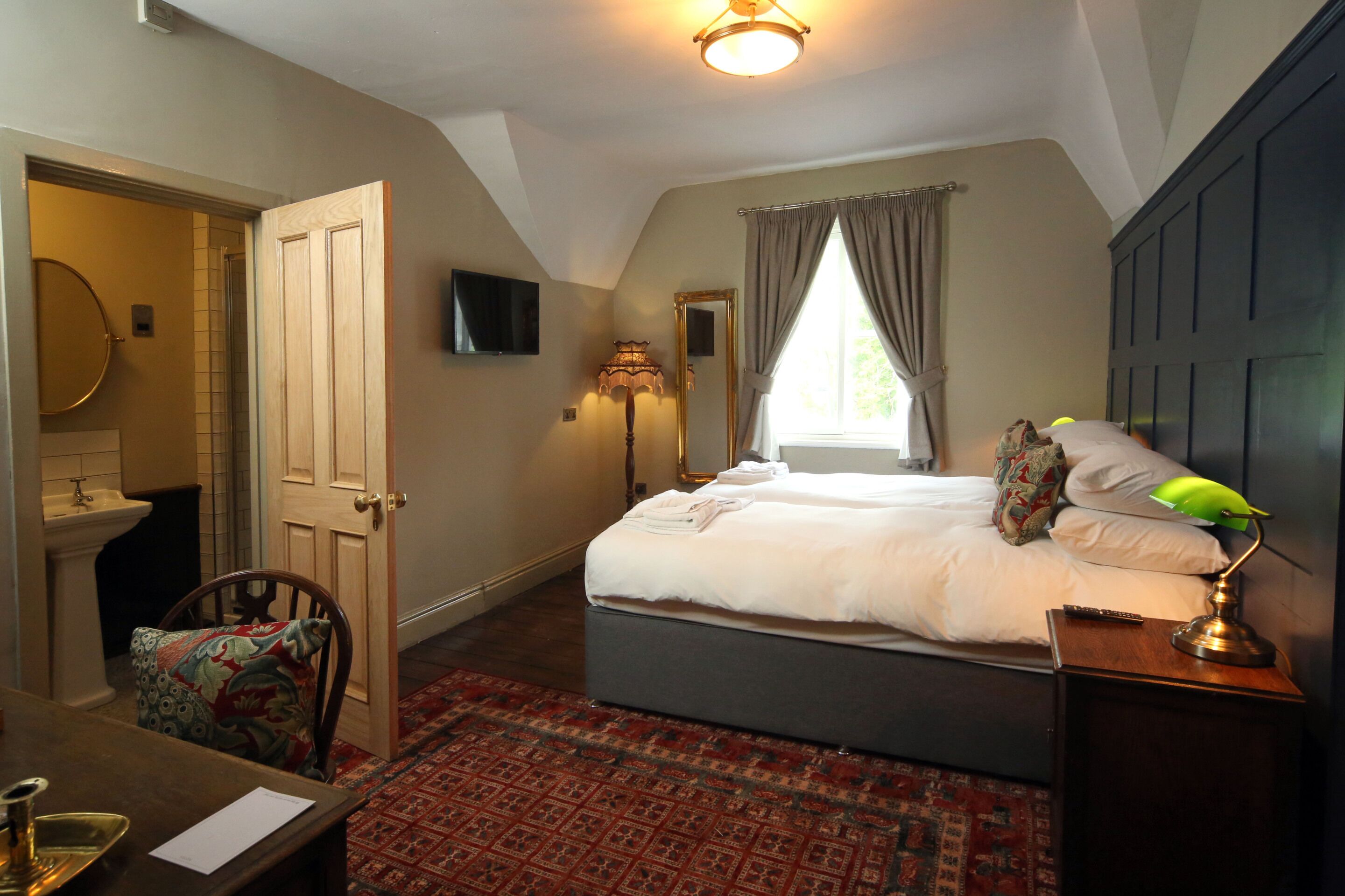 A bedroom with a bed, bedside table, lamp, and a view of the outdoors through a window.