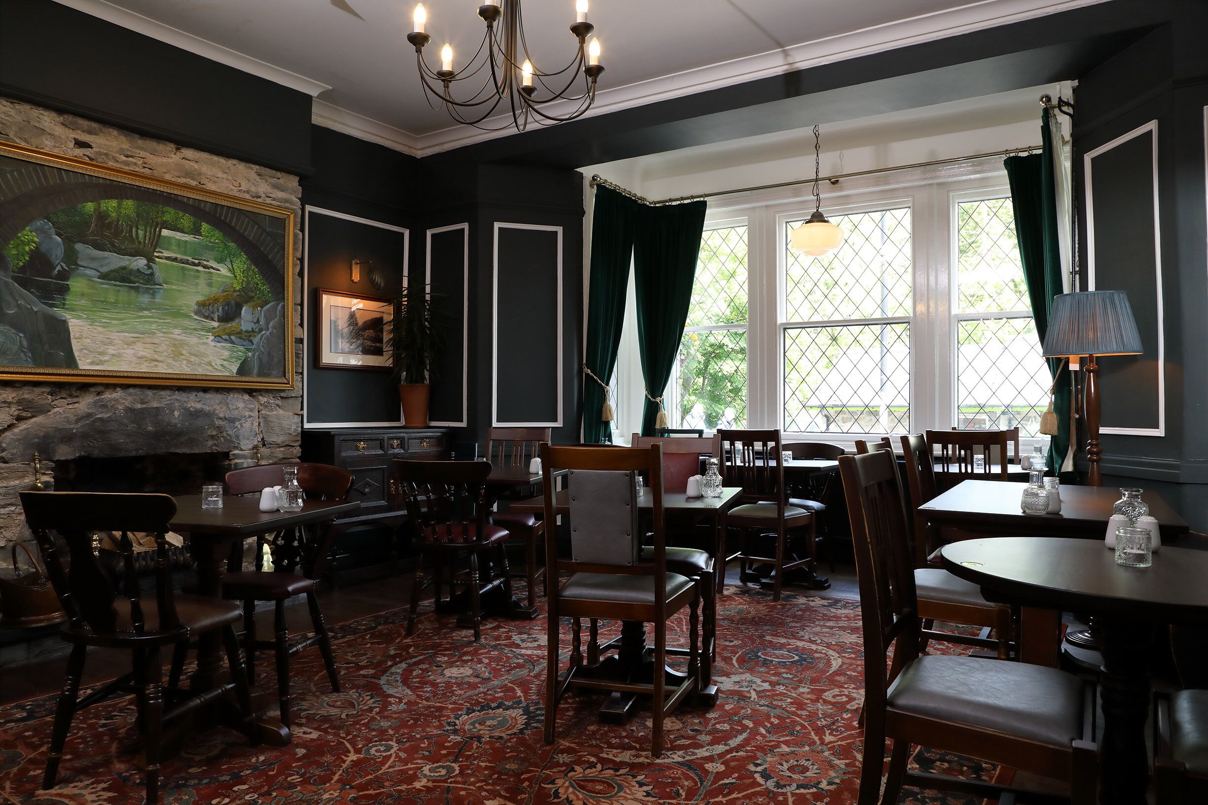 A dining area with wooden tables and chairs, a chandelier, and a large painting on the wall.
