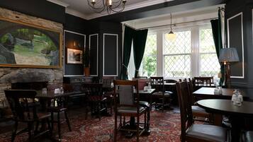 A dining area with wooden tables and chairs, a chandelier, and a large painting on the wall.