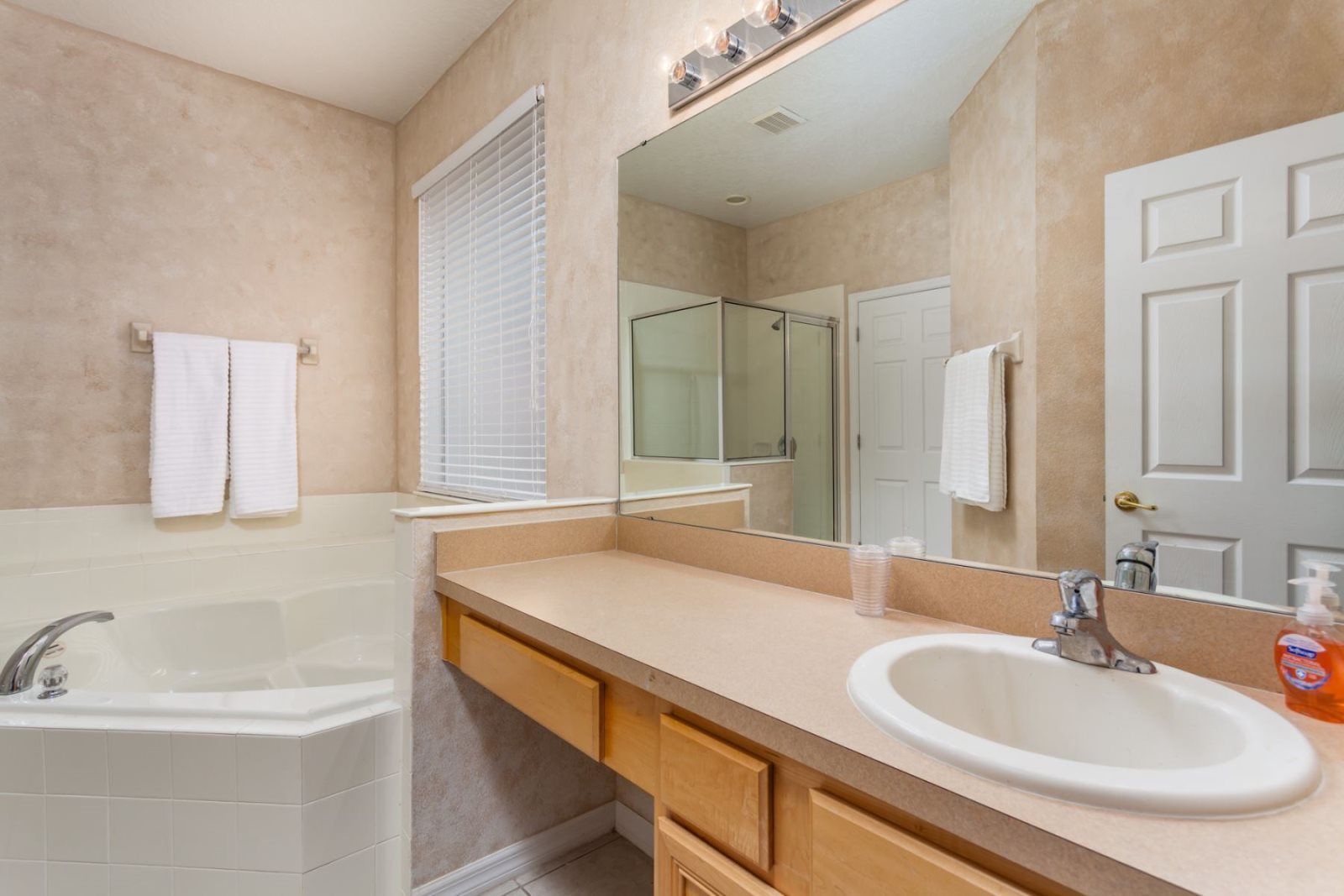 A bathroom with a bathtub, a sink, a mirror, and a window with blinds.