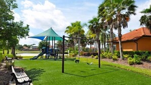A playground with swings and a slide, surrounded by palm trees and a grassy area. - 4 Br Pool Home in Aviana Resort (Davenport)