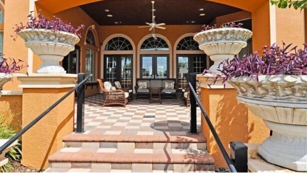 A covered outdoor seating area with a checkered floor, a staircase, and two large planters with purple flowers. - 4 Br Pool Home in Aviana Resort (Davenport)