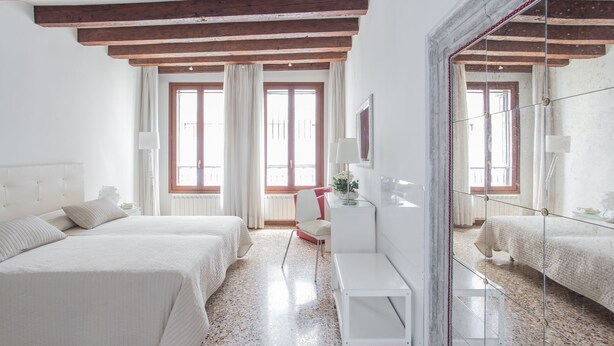 Ein Schlafzimmer mit Bett, Nachttisch, Spiegel und einem Fenster mit Vorhängen.