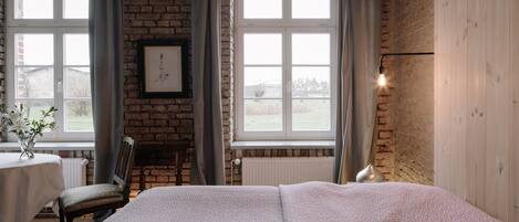 A bedroom with a large bed, a wooden wardrobe, a brick wall, and a window with curtains.