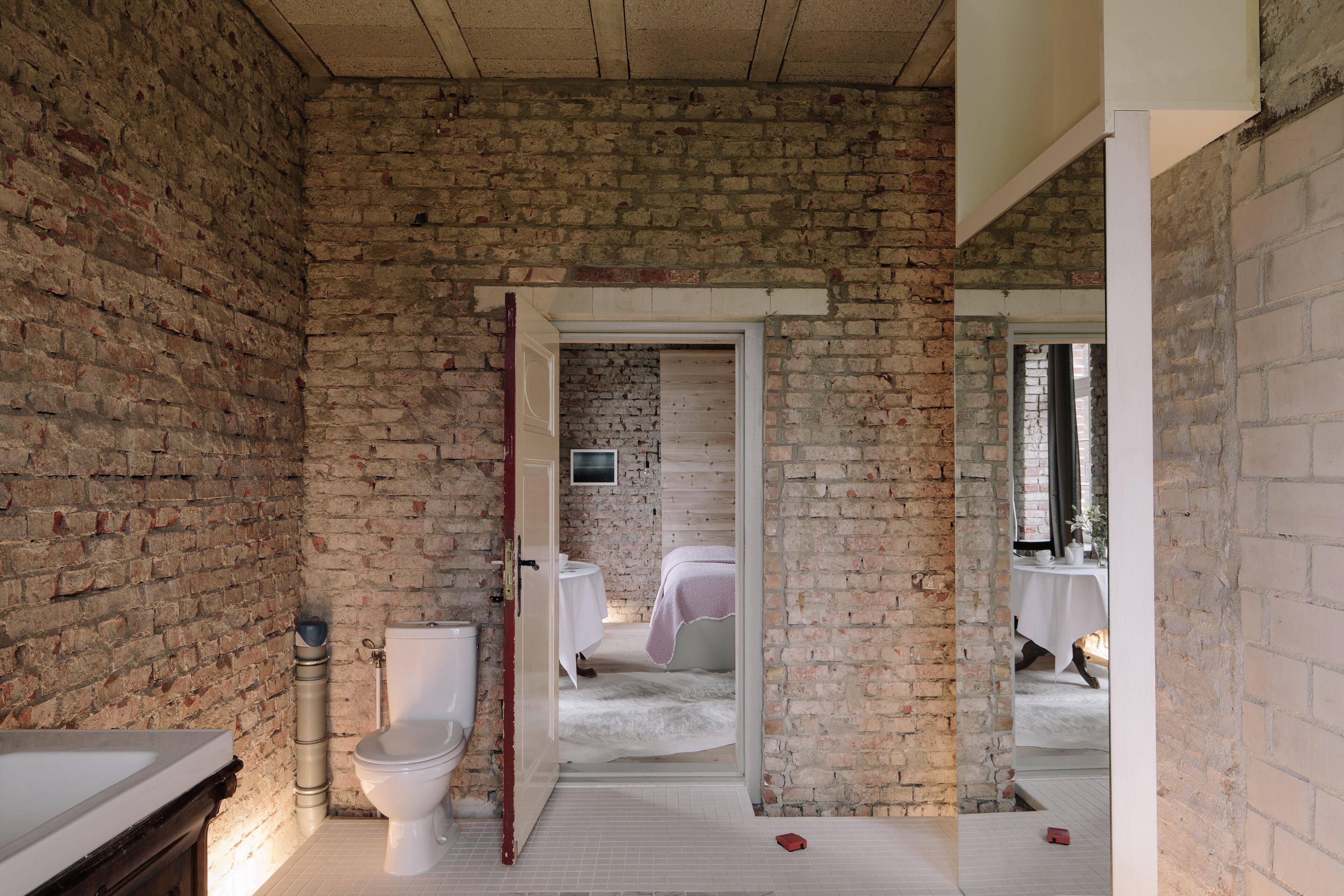 Een badkamer met een bakstenen muur, een wit bad, een toilet en een bed met een roze deken.