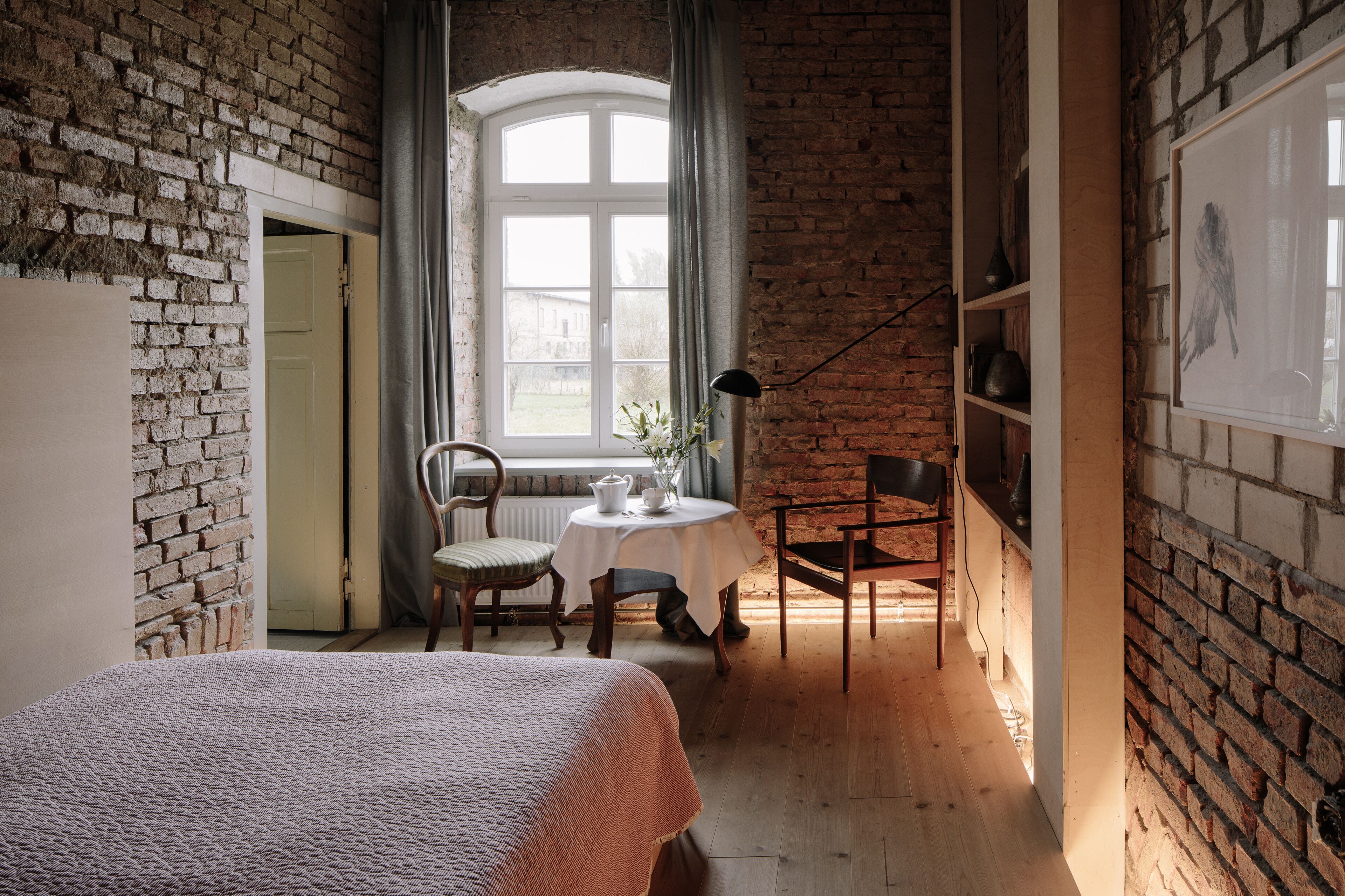 Une pièce avec un mur en briques, un lit, une table avec des chaises et une fenêtre avec des rideaux.