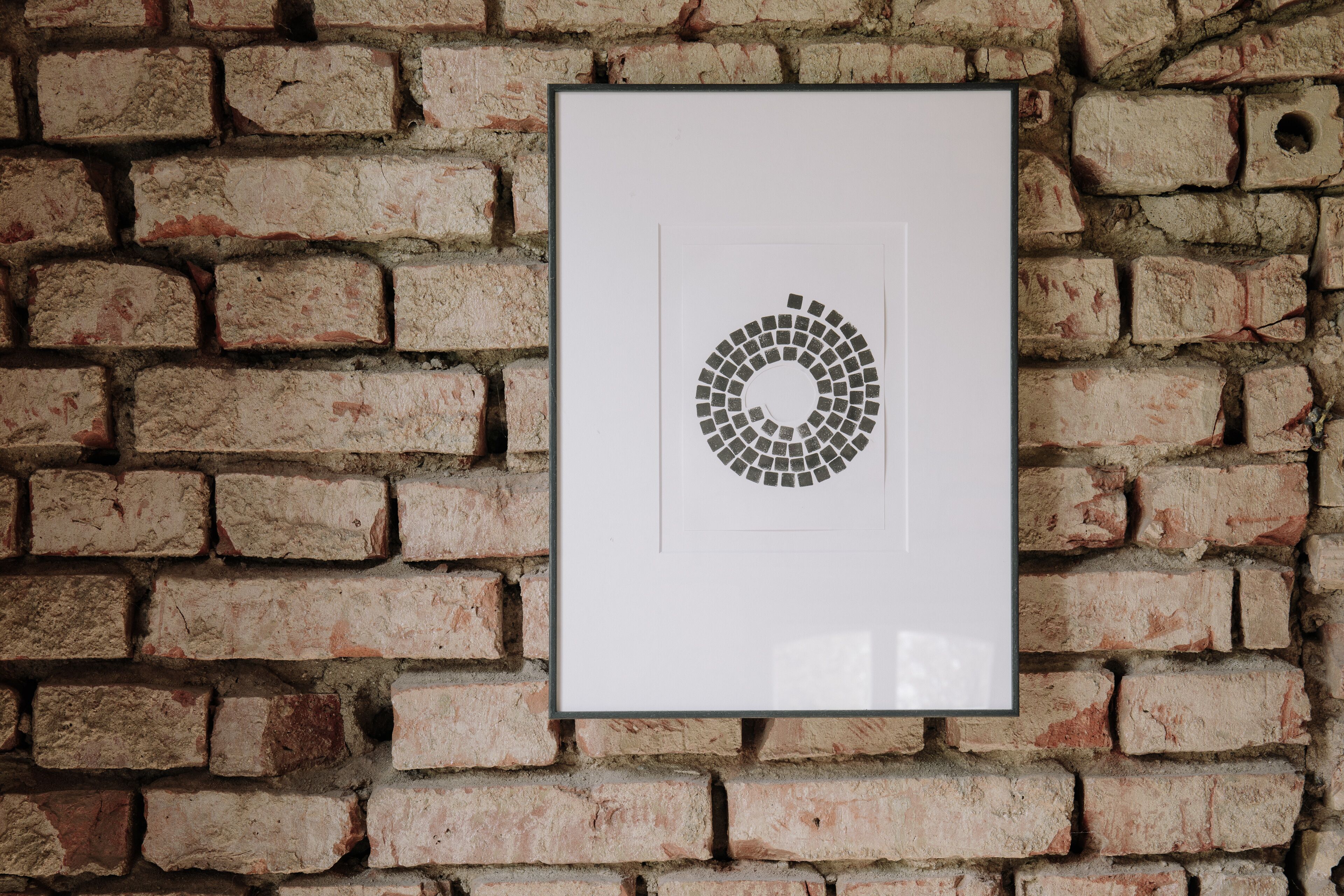 Een lijstwerk met een cirkelvormig mozaïekpatroon op een bakstenen muur.