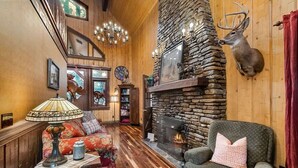 Ein gemütliches Wohnzimmer mit Kamin aus Stein, Holzwänden und einem aufgehängten Hirschkopf.