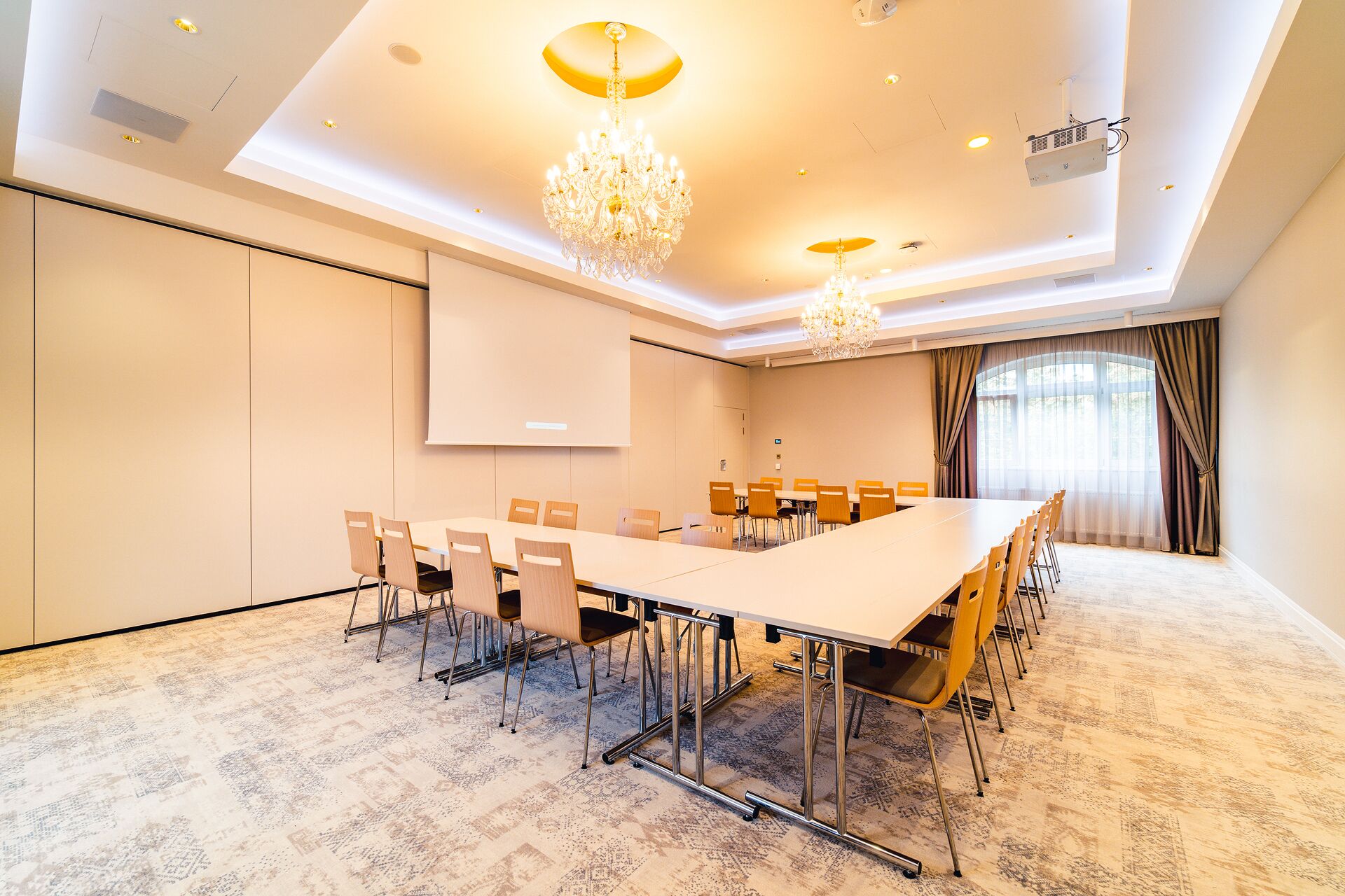 A conference room with a long table, chairs, a projector screen, and a chandelier.