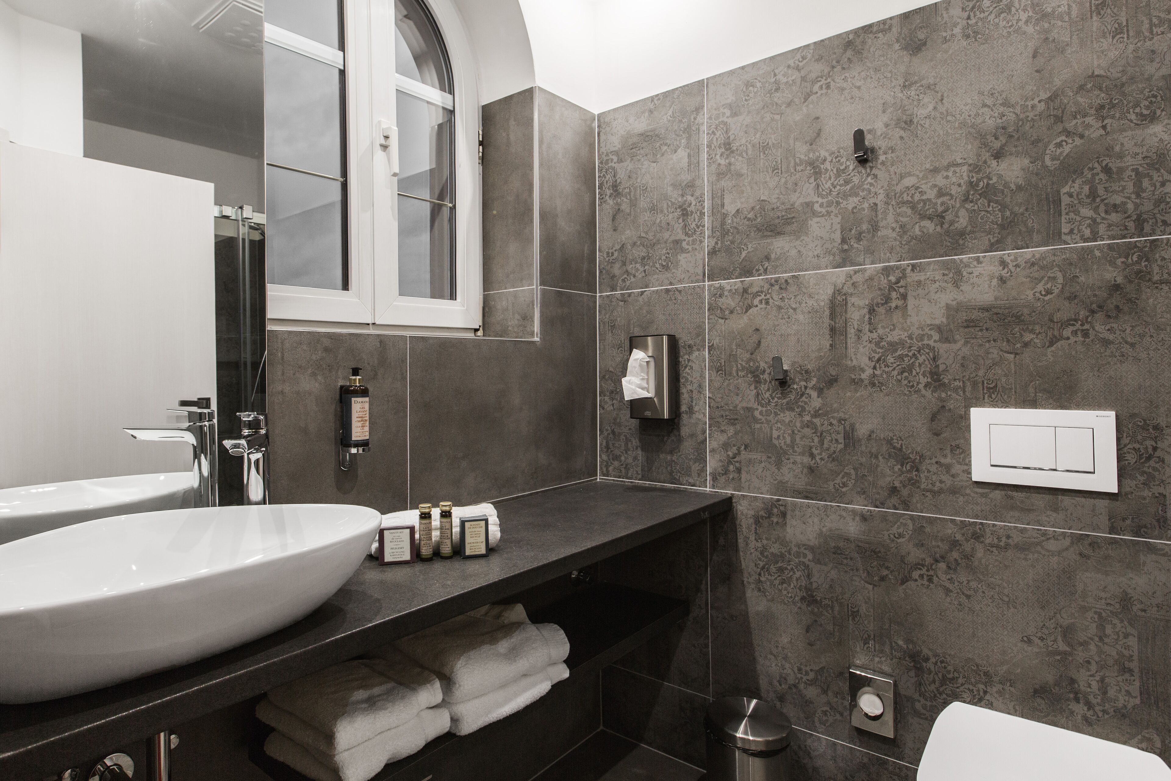 Un baño moderno con un lavamanos grande y blanco, paredes de baldosas oscuras, un espejo y una ventana.