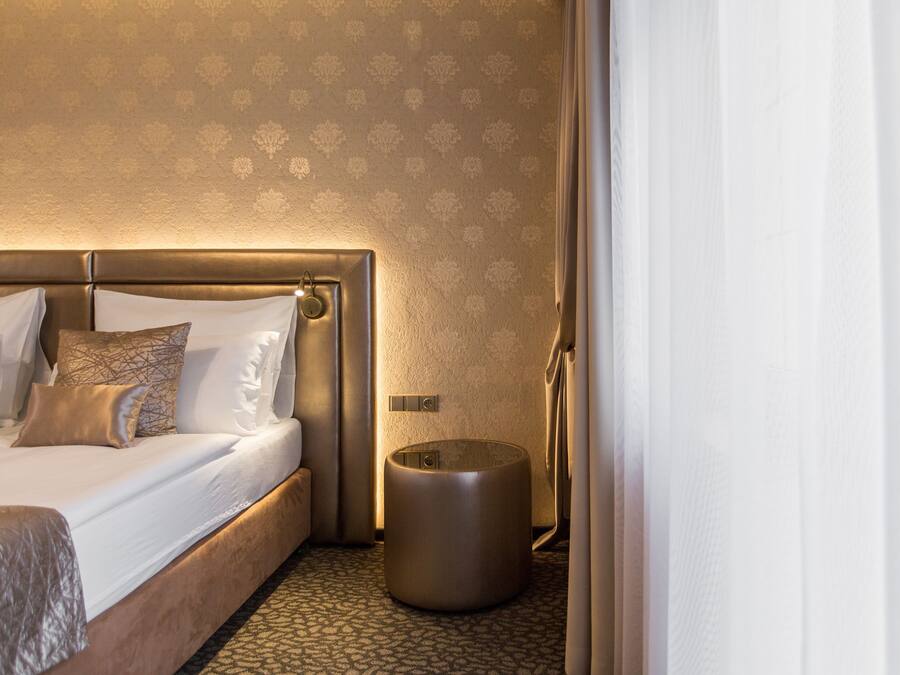 Quarto de hotel com uma cama grande, um banquinho redondo e um tapete estampado.