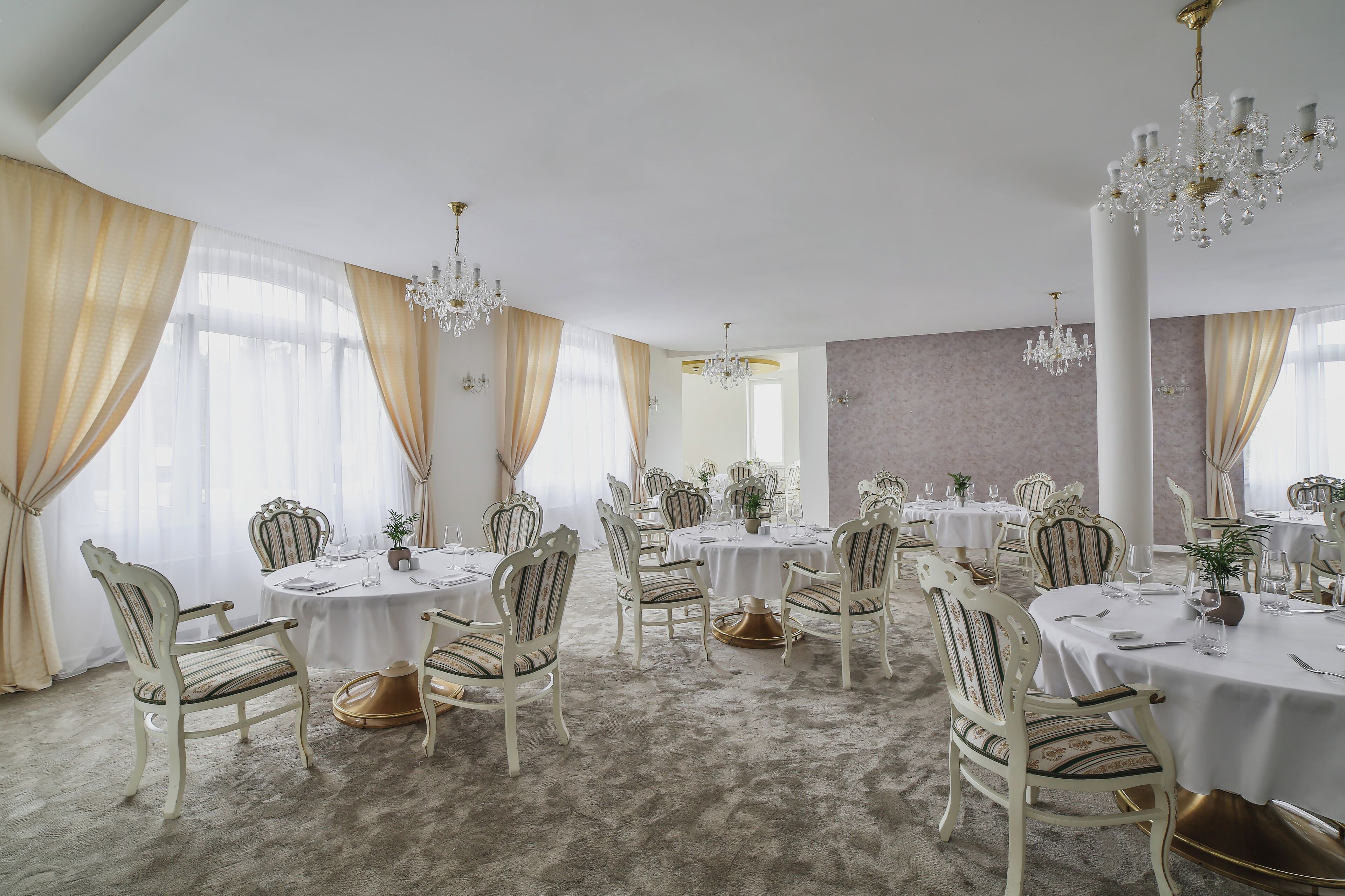 A formal dining room with round tables, ornate chairs, and chandeliers.