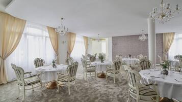 A formal dining room with round tables, ornate chairs, and chandeliers.