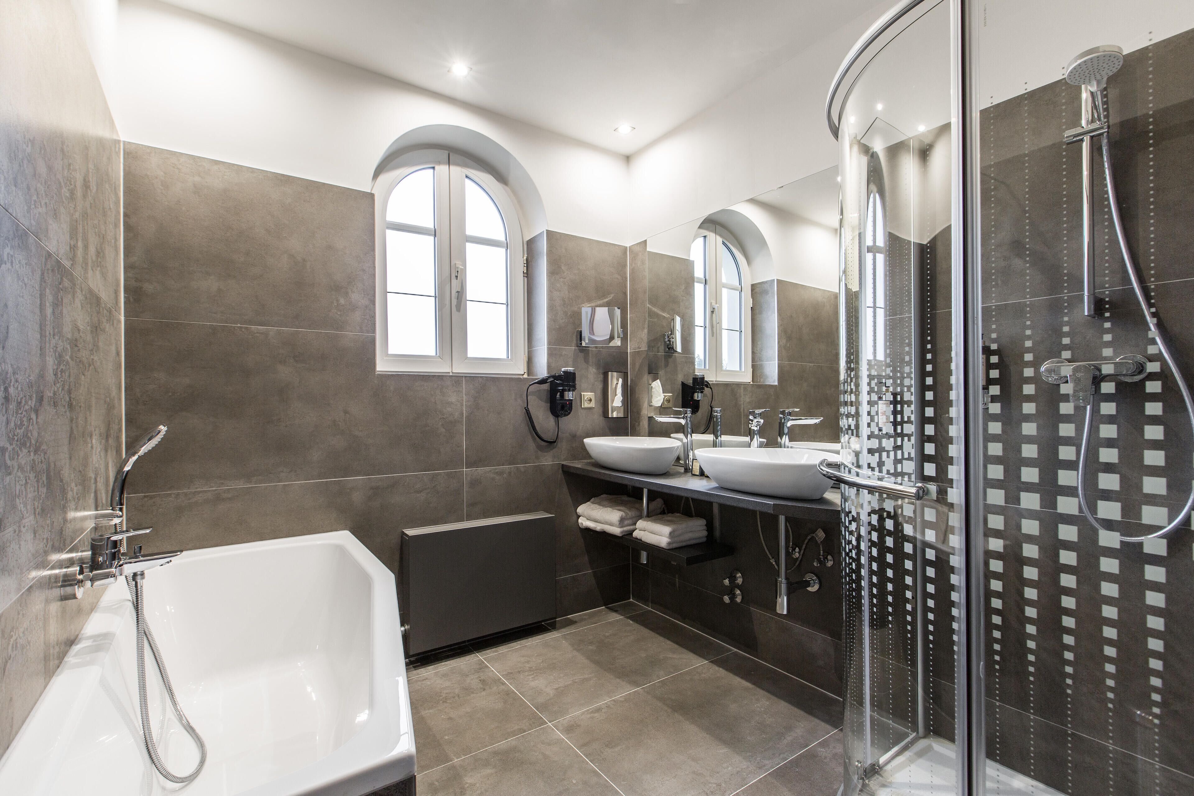 Ein modernes Badezimmer mit Badewanne, zwei Waschbecken, einer Duschkabine aus Glas und einem großen Spiegel.