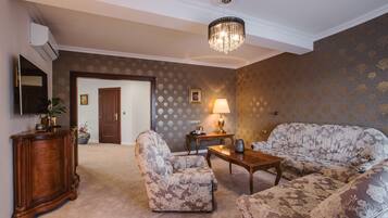 A living room with a sofa, armchair, and a wooden coffee table. There is a door leading to another room, a lamp on a side table, and a decorative vase.