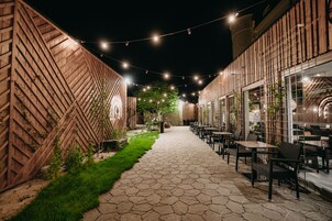 Un patio al aire libre con un camino de piedra, paredes de madera y luces colgantes.