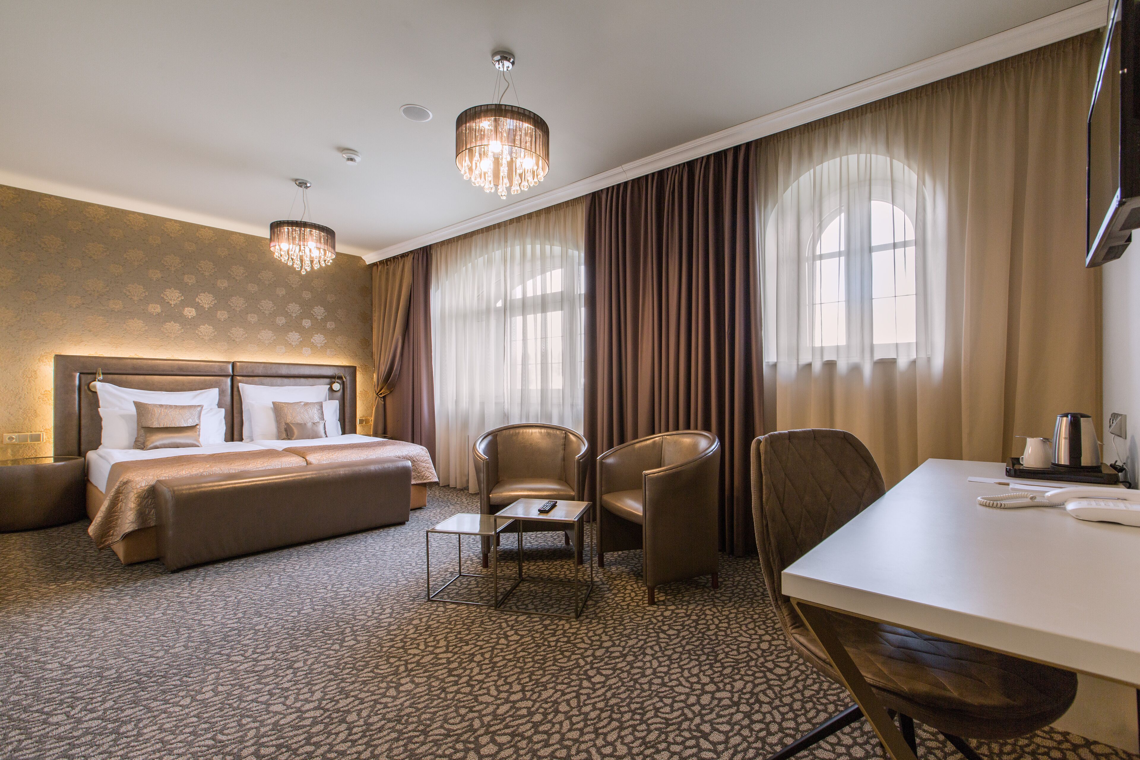 A hotel room with a king-sized bed, two armchairs, a small table, and a desk with a telephone.