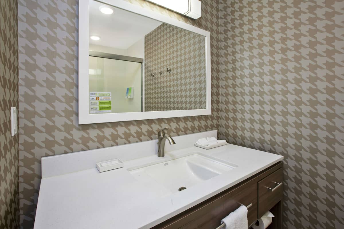Un baño con lavamanos blanco, espejo y perchero.