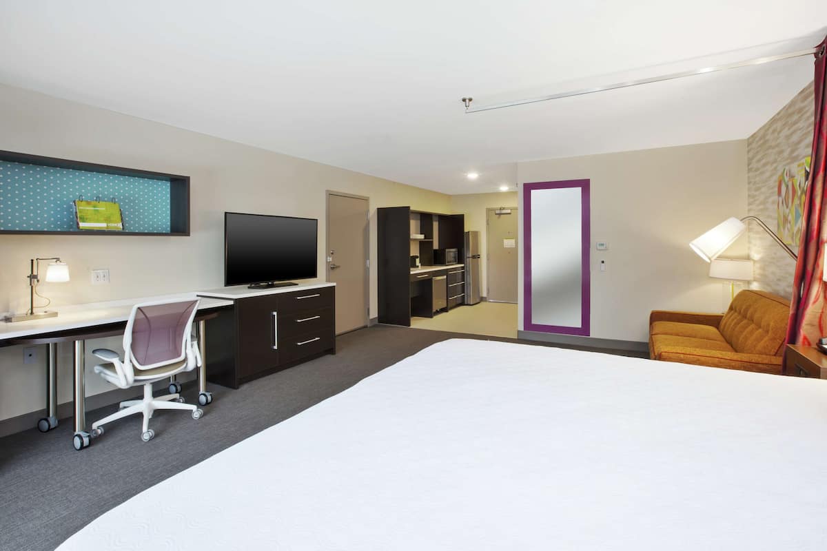 Habitación de hotel con una cama grande, un escritorio con silla, televisor, armario, espejo y sofá.