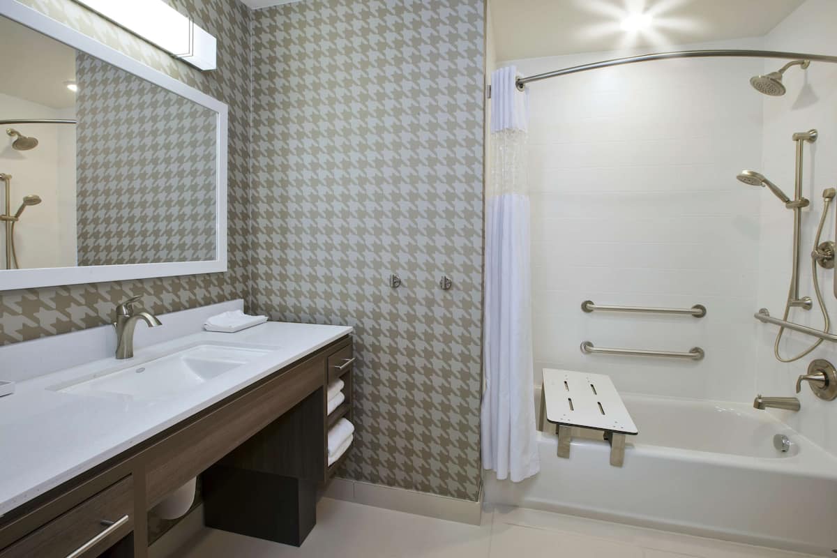 Un baño moderno con dos lavamanos, ducha con barras de apoyo y un espejo sobre el lavamanos.